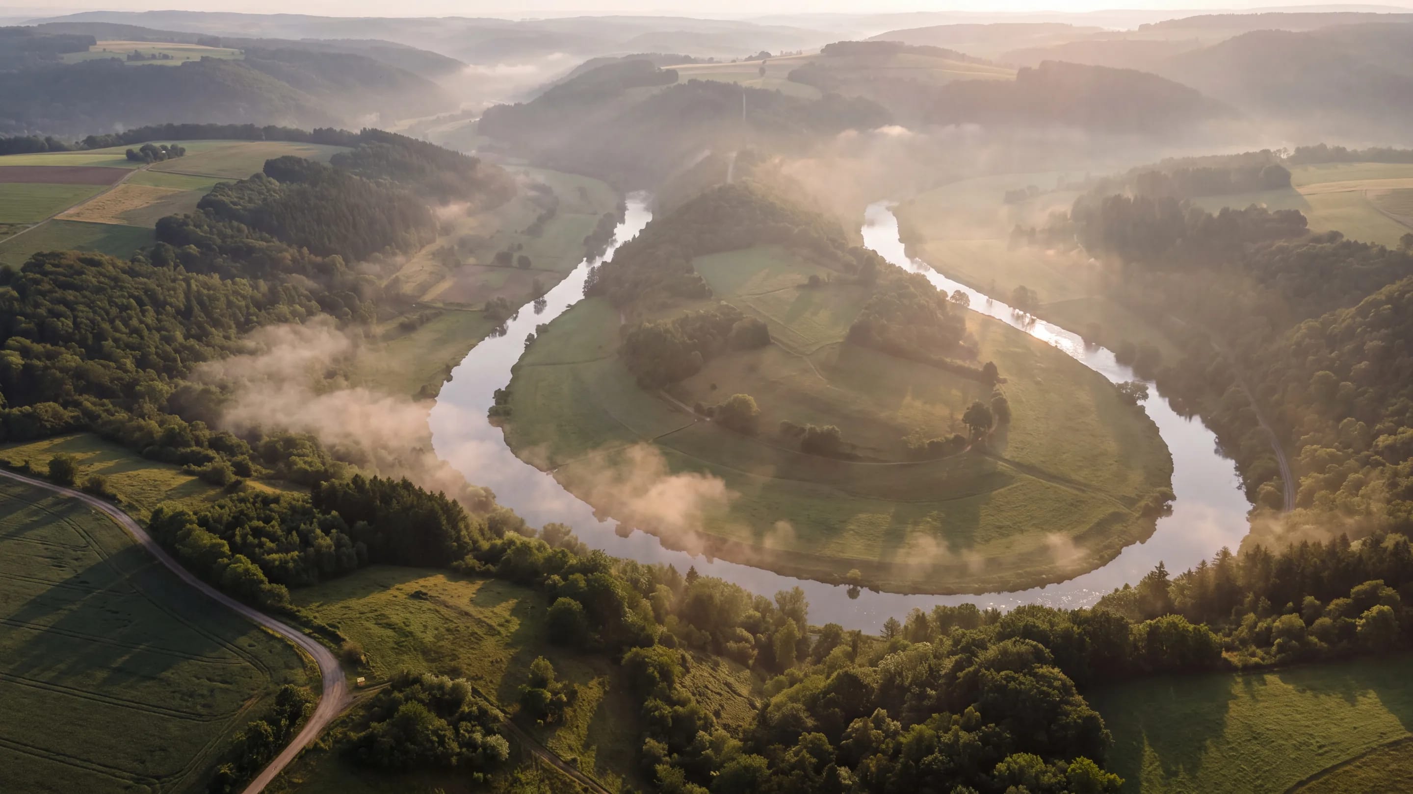 Ein breiter Fluss aus der Luft, der sich durch eine Tallandschaft zieht, Morgenlicht auf dem Wasser.