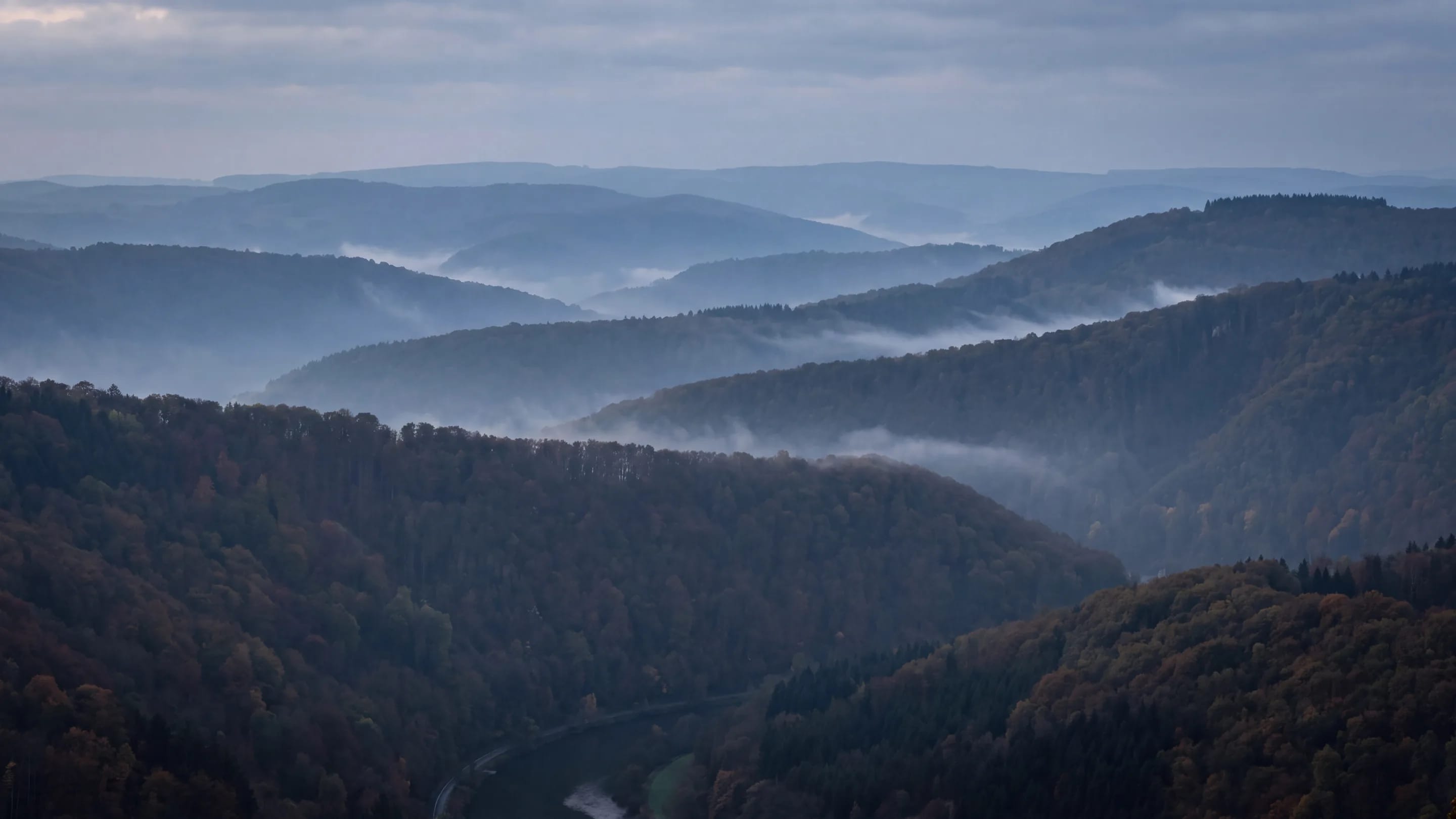 Mehrere bewaldete Bergkuppen hintereinander gestaffelt, im Dunst des frühen Morgens.