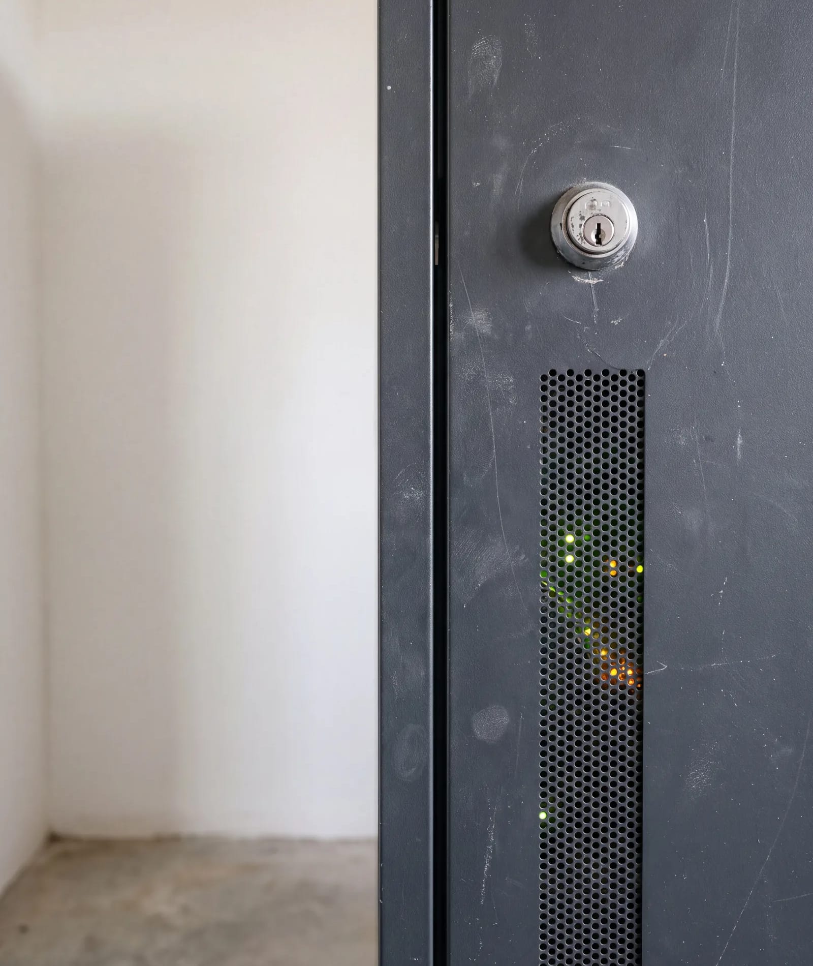 Ein verschlossener Serverschrank, hinter der Glastür leuchten die Statusanzeigen der Geräte.